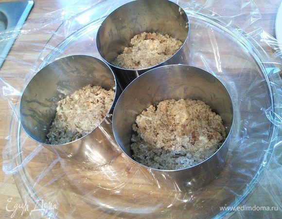 Удобную форму выложить плёнкой, установить в неё формочки. Хлебцы мелко покрошить и перемешать с размягченным маслом. Равномерно выложить смесь в виде основы в подготовленные формы, утрамбовать и поставить в холодильник. 