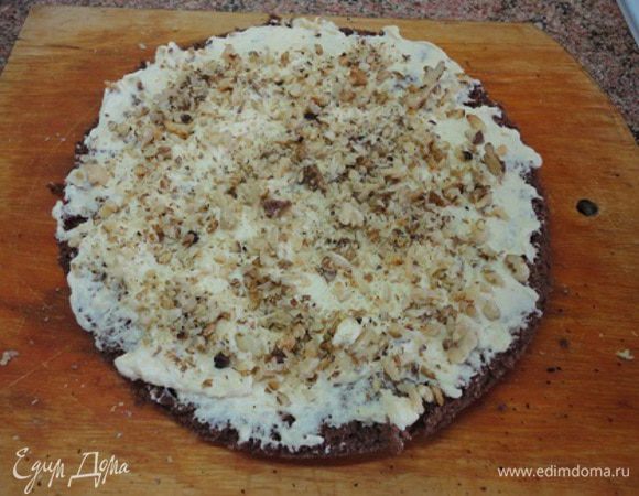 Собирать торт начинаем с темного коржа — смазываем кремом и посыпаем половиной орехов.