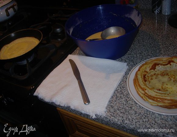 Дайте тесту несколько минут отдохнуть, а за это время подготовьте рабочее место.
Понадобиться антипригарная сковорода с ручкой, половник, нож с тупым концом, плоская тарелка или стеклянная разделочная доска.
Разогрейте хорошо сковороду, затем убавьте огонь в положение "чуть меньше среднего", если сомневаетесь, то для первого блина предварительно смажьте сковороду растительным маслом или сливочным маслом наколотым на вилку.
Половником еще раз слегка перемешайте тесто, зачерпните нужное количество, ориентируясь на размер сковороды, поднимите сковороду с плиты и навесу влейте тесто на сковороду. Наклоняя сковороду в разные стороны заполните дно, кладите ее обратно на плиту, но далеко не уходите. Блинчики жарятся быстро.
Как только край подрумянился поддеть его ножом и переверните блинчик аккуратно держа пальцами обеих рук. 
Постарайтесь не обжечься. 

Обжаривать со второй стороны нужно еще меньше времени, чем с первой.
Снимайте с огня на тарелку (можно прикрыть широкой крышкой или миской, так блины получатся еще нежнее и не будет сухих краев) и продолжайте жарить.