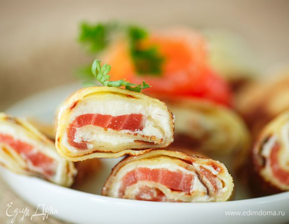 Готовые блинчики смазываем творожным сыром. Выкладываем на смазанный блинчик ломтики дикого лосося. Сворачиваем блинчик и нарезаем на роллы 3-4 см. Украшаем веточкой зелени. Приятного аппетита! 