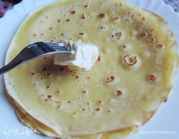 Каждый блинчик выкладываем на тарелку и сразу же смазываем кусочком сливочного масла. Я беру масло из холодильника, накалываю на вилочку кусочек и смазываю им блинчик.