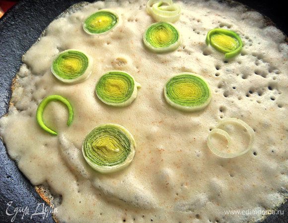 Налить на разогретую и промазанную маслом чугунную сковороду тесто и сразу расположить сверху лук.