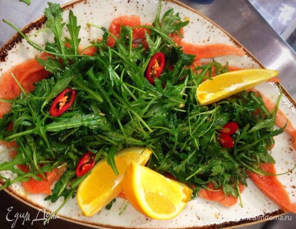 Чтобы остановить процесс приготовления рыбы, выложить на нее руколу и вылить все остатки заправки. Ароматы рыбы, заправки, оливкового масла быстро перемешаются на теплой тарелке. Посыпать карпаччо крупной солью, розовым перцем и крупно нарезанным апельсина и подавать. Приятного аппетита!