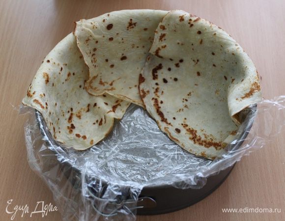 Форму 20 см проложить пищевой плёнкой, чтобы середина не была ею застелена и чтобы плёнка свисала по краям (я застелила всю форму и было трудно убрать пленку, не делайте так). Выложить в форму  блины внахлёст, чтобы их края  свисали из формы.