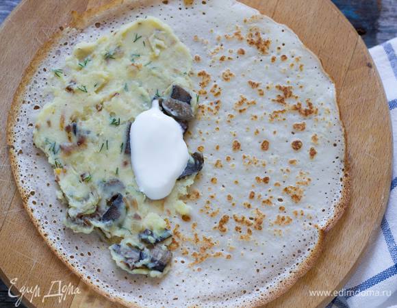 Выложите 1 ст. л. грибной начинки и 0,5 ч. л. сметаны на половину блинчика, накройте его другой половинкой, затем сверните еще раз, чтобы получился треугольник.