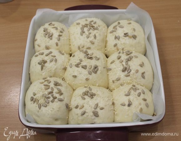 Когда заготовки подрастут, смазываем булочки молоком и присыпаем их семенами.
