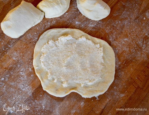 Подошедшее тесто выложить на рабочую поверхность, обмять. Разделить на шарики и каждый расплющить в лепёшку. Намазать на всю поверхность лепёшки начинку.