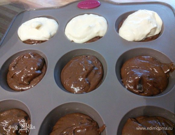 Форму для маффинов выложить бумажными прокладками, рекомендую это сделать, т. к. бумажные формочки имеют больший объем и они чуть выше. Разложить тесто, а поверх теста по полной столовой ложке сливочного крема.