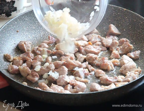 Когда мы видим золотистую корочку на кубиках мяса, добавляем растительное масло из нашего стаканчика и выкладываем к мясу порезанный лук.