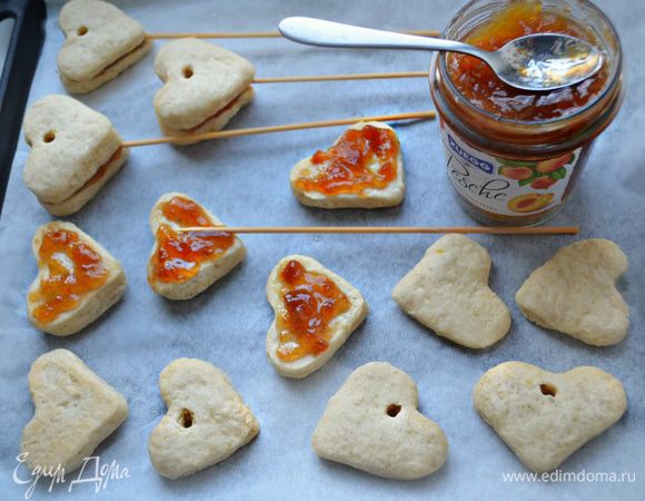После чего выньте заготовки из духовки. В половине из них сделайте с помощью коктейльной трубочки небольшое отверстие в центре. Смажьте нижнюю сторону печенья джемом, немного, чтобы в процессе выпекания джем не вытек (я использовала персиковый джем). Положите длинную деревянную шпажку по центру печенья (лучше заранее подготовить шпажки, замочив на 15 -20 мин в воде), сверху — вторую половинку и слегка прижмите. 