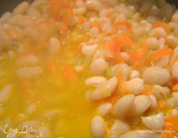 В сковороду с овощами выложить половину отваренной фасоли, перемешать, влить немного горячего куриного бульона и все прогреть.