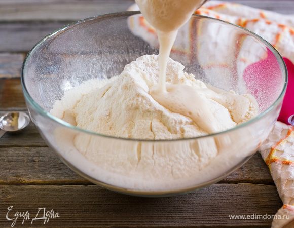 В центре горки сделайте углубление. Влейте дрожжи, добавьте разрыхлитель и начните постепенно замешивать, затем небольшими порциями вливайте оставшуюся теплую воду (210 мл) и вымешивайте тесто силиконовой лопаткой.