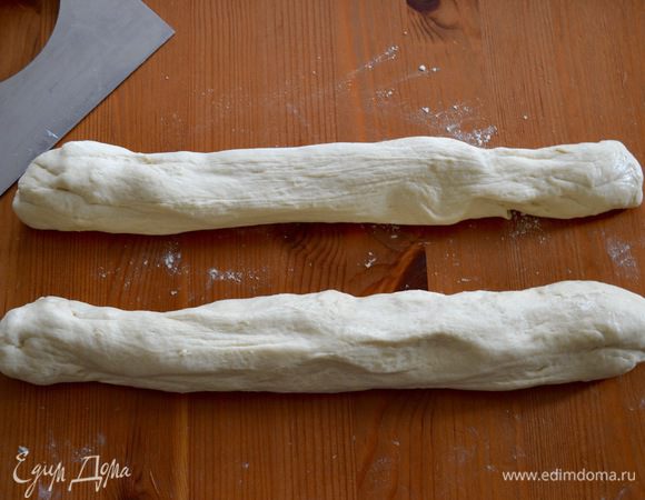 Выложить воздушное и очень податливое тесто на рабочую поверхность, слегка присыпанную мукой, и разделить на две части, смазав руки оставшимся маслом. И опять облегчаем себе процесс приготовления багетов, т. к. мы не будем раскатывать и скручивать багеты, а просто растянем каждый кусочек теста в длину — быстро и просто. Выложить багеты на противень, застеленный пекарской бумагой и присыпать слегка мукой. Накрыть полотенцем и дать отдохнуть еще буквально 15 минут.