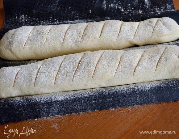 За это время включаем разогреваться духовку на 195ºC. Тем временем, багеты заметно увеличились... Сделать на поверхности поперечные косые надрезы острым лезвием и поставить выпекаться в горячую духовку ровно на 15 минут. Важно — под противень предварительно поставить форму с кипятком и стенки духовки сбрызнуть водой, прежде чем поставить багеты на выпечку.