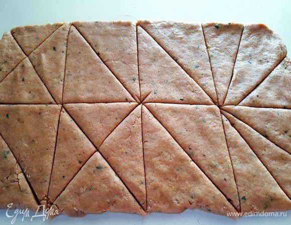 Выложить тесто на припудренную мукой поверхность, сформировать из него форму прямоугольника, и используя скалку, раскатать более большой формат прямоугольника толщиной примерно 13-18 мм (у меня получился размер прямоугольника 25х35 см).

Используя нож-ролик для пиццы или обычный нож порежьте пласт теста примерно на 10-12 одинаковых прямоугольников, далее разрежьте каждый прямоугольник на 2 треугольника (размеры сконов вы можете варьировать произвольно и индивидуально).
