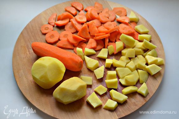 Помойте и почистите морковь и картофель. Картофель нарежьте кубиками или небольшими кусочками, морковь — кружочками. Сложите в кастрюльку.