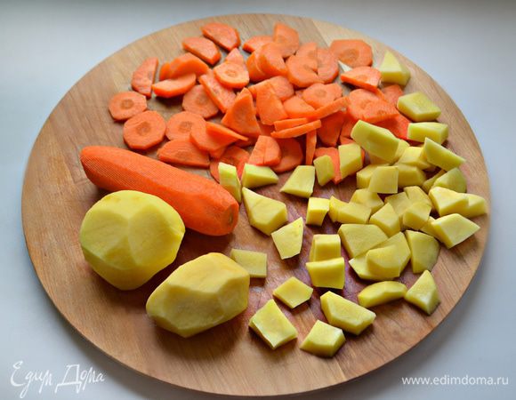 Помойте и почистите морковь и картофель. Картофель нарежьте кубиками или небольшими кусочками, морковь — кружочками. Сложите в кастрюльку.