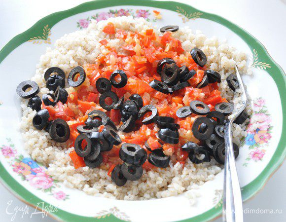 Включить разогреваться духовку до 180°С.
Маслины нарезать кружочками. Выложить приготовленные овощи к крупке, посолить и поперчить по вкусу, перемешать.