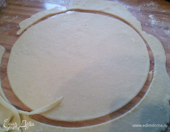 Приблизительно 1/4 часть теста отставить в сторону (это будет "крышка" пирога). На посыпанной мукой поверхности раскатать тесто, выдавить донышком от разъемной формы (26 см в диаметре) круг. Саму форму выложить пергаментом.