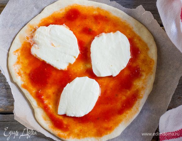 Раскатайте тесто в тонкий пласт. Круглую форму для выпечки смажьте оливковым маслом, переложите в нее тесто, равномерно смажьте основы томатным соусом, сверху разложите моцареллу.