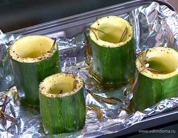 Форму выстелить пищевой фольгой, поместить на нее цукини выемками вверх, посолить, поперчить, сбрызнуть оливковым маслом, посыпать листьями розмарина и запекать под хорошо разогретым грилем 5‒7 минут.