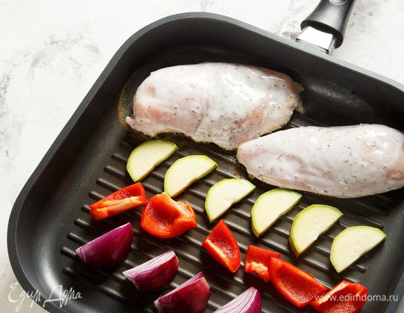 Красный лук, кабачки и болгарский перец нарезать. Достать из холодильника курицу. Выложить курицу и подготовленные овощи на гриль, обжарить до готовности.