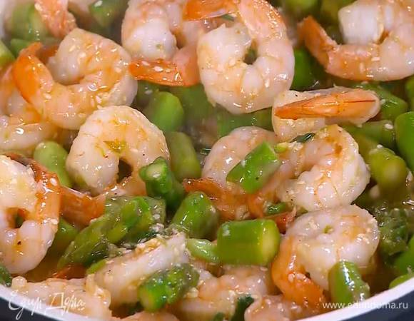 К креветкам со спаржей добавить кунжутное семя, зеленый лук, все перемешать, влить заправку, снова перемешать и прогревать еще около минуты.