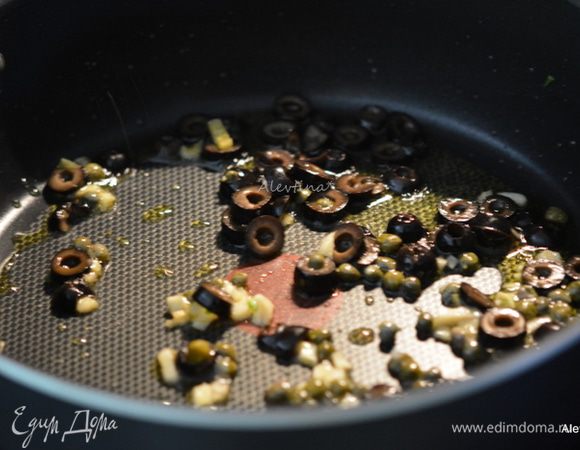 Разогреть оливковое масло. Добавить очищенный и нарезанный чеснок, каперсы, оливки желательно каламата. Готовить примерно 2 мин.