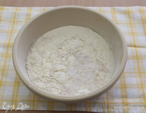 Просеять в миску муку 500 г и добавить разведенные дрожжи. Тщательно перемешать. Накрыть и поставить в теплое место на 30-40 минут.