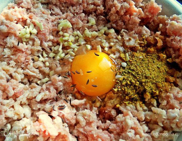 В фарш вбить яйцо, выдавить или порубить чеснок, всыпать тмин и смесь приправ (горчица, чили, базилик, морковь, лук, куркума).