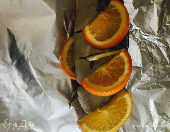 Затем во внутрь разрезанной рыбы положить розмарин, тимьян и несколько кусочков апельсина. И также в надрезы положить по кусочку апельсина.