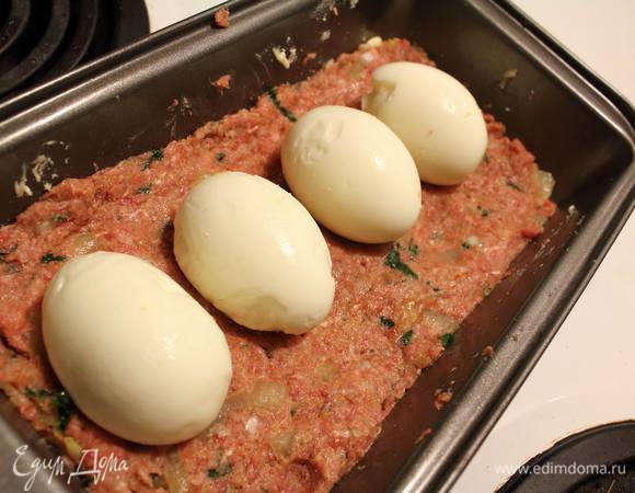 Форму для хлеба смазать маслом, выложить половину фарша, уложить вареные почищенные яйца, накрыть оставшимся фаршем и отправить выпекаться в разогретую до 180°C духовку. На 50-60 минут. 
Где-то через 40 минут я слила вытекший жир и еще на последние пару минут включила функцию гриль.