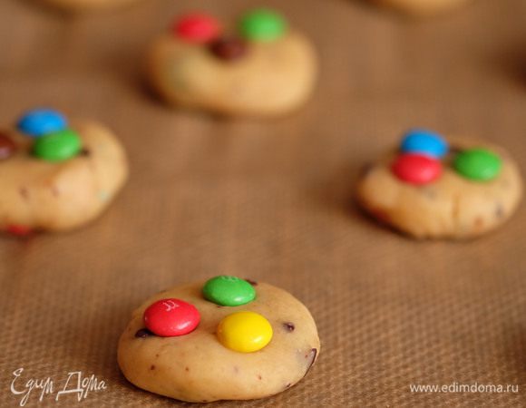 Разогреть духовку до 180°C. Достать тесто из холодильника и формировать печенья: отщипнуть небольшой кусочек теста, скатать шарик (величиной примерно с грецкий орех), сплющить его до толщина 1-1,5 см и уложить на противень, застеленный бумагой для выпечки. Сверху вдавить 2-3 конфетки. Таким образом сформировать печенья из оставшегося теста.