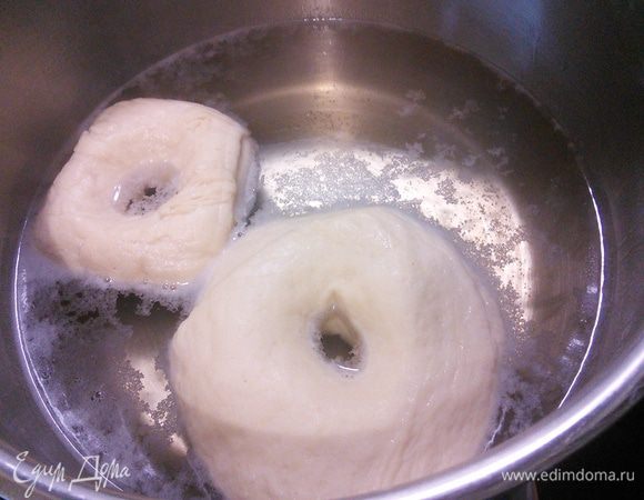 В большой кастрюле разведите ложку меда в 1 литре воды, доведите до первых пузырьков и окуните бублик в воду с каждой стороны по 1 минуте. Удобно это делать с помощью большой шумовки. За один раз у меня получилось "искупать" по 2 бублика. 