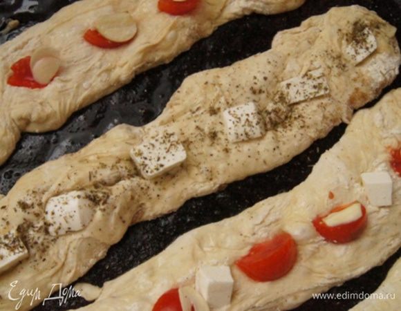 Доску опять присыпать мукой, переложить тесто, разделить его на 4 части. Я делала это силиконовой лопаткой. 
Слегка растягивая тесто, перенести 4 батончика на смазанный маслом противень. У меня получились не очень ровненькие, но на вкус это не повлияло.

Начинка для такого может быть любой. Я порезала помидорки черри на четвертинки, чеснок слайсами, фету кубиками. Распределить начинку поровну между хлебом.
Смазать каждую стекку кисточкой оливковым маслом (у меня растительное). Если не используете фету, то присыпьте морской солью. По вкусу присыпьте прованскими травками.
Пока духовка разогревается, стекки немного подойдут.