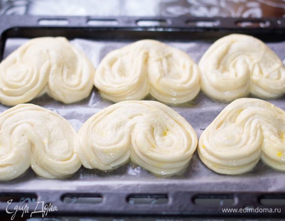 Заготовки-плюшки выкладываем на противень, застеленный бумагой для выпечки или смазанный растительным маслом. Плюшки очень сильно увеличатся в объеме, так что расстояние между ними оставляйте не малым.
Смазываем заготовки смесью из желтков, молока и сахара. Ставим в теплое место на расстойку, на 30 минут. Чтобы плюшки не подсохли сверху, нужно накрыть их смазанной растительным маслом пленкой.