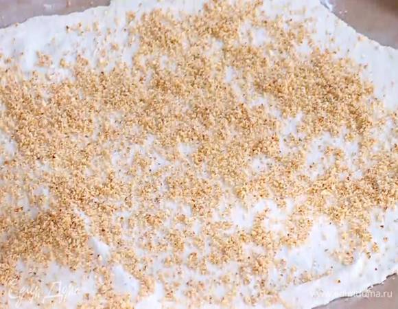 Тесто раскатать на бумаге для выпечки в очень тонкий прямоугольный пласт и посыпать частью измельченного миндаля.