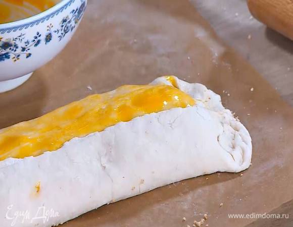 Смазать желтком край теста изнутри и плотно прижать к рулету, затем смазать весь рулет желтком и защипнуть тесто по краям.