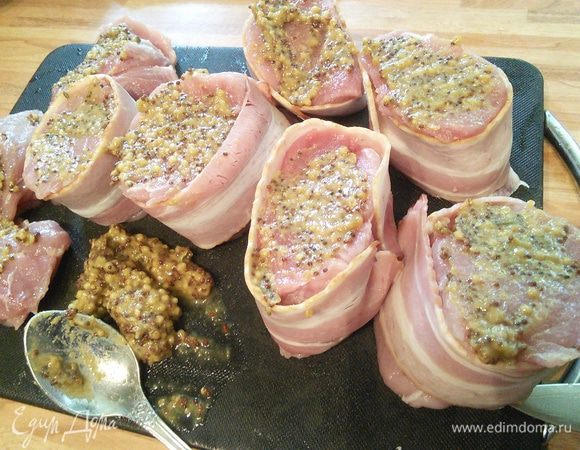 Каждый медальон обернуть полоской бекона, со обеих сторон мяса смазать горчицей и уложить медальоны на лук. Духовку разогреть до 200°С. 