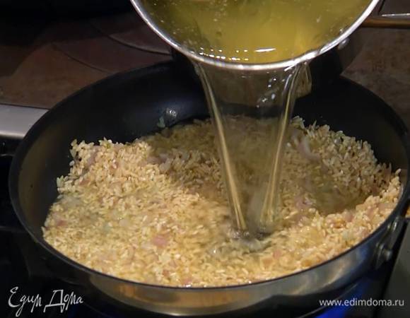 Рис всыпать в сковороду с луком и чесноком, перемешать и дать ему пропитаться маслом, влить пару половников куриного бульона, все перемешать, затем влить еще куриного бульона, так чтобы рис был полностью покрыт, и прогревать на небольшом огне до готовности.