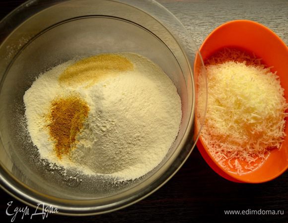 В миску просеять муку, добавить семолину (или манную крупу), сахар, соль, разрыхлитель и немного шафрана (или куркумы). Натереть на мелкой терке сыр и добавить к остальным сухим продуктам, перемешать.