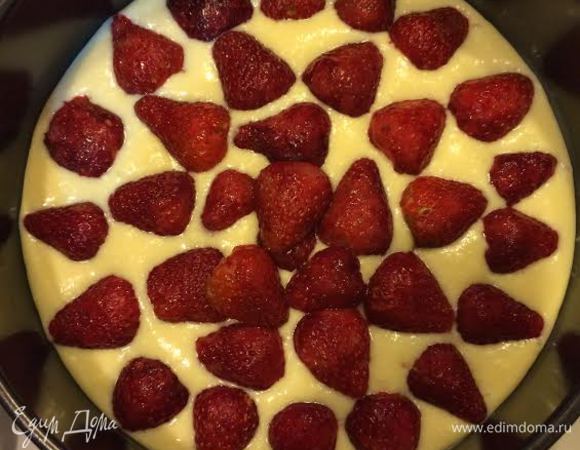 Форму диаметром 20 см смазать маслом и вылить половину теста. Клубнику порезать пополам и уложить в форму.