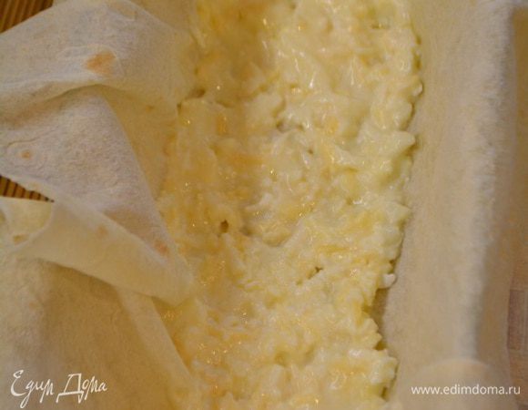 Сливочное масло растопить. Взять форму и застелить ее лавашем, чтобы края свисали. Смазать с помощью кисточки растопленным сливочным маслом. Выложить сырную начинку, разровнять.