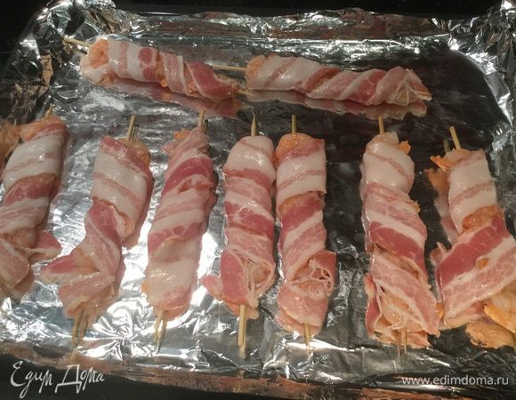 Каждую шпажку оберните в бекон и жарьте на открытом гриле или в духовке на режиме "гриль", по 3-4 минуты с каждой стороны, бекон должен подрумянится. 