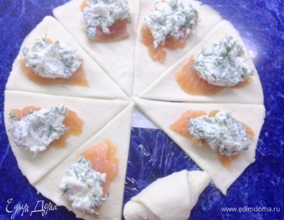 Из 500 г теста у меня получилось вырезать три таких круга для круассанов (получилось 24 штучки). Делим тесто на сегменты. Выкладываем по кусочку рыбы, а сверху ложечку сырной начинки. Сворачиваем круассаны.