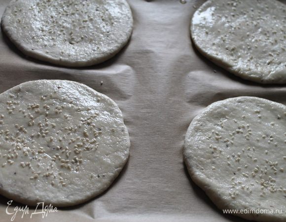 Через час тесто обмять и разделить на 4 части. Раскатать в лепешки (10 см в диаметре), смазать растительным маслом и посыпать кунжутом. Накрыть пленкой и оставить на 20 минут.