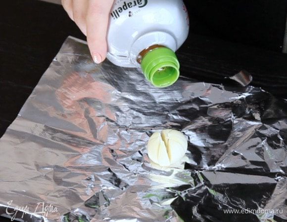 Разогреть духовку до 200°C. Полить чеснок маслом, завернуть в фольгу и запекать 30 минут. Остудить 10 минут перед добавлением в масло.