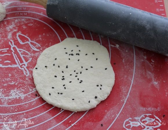 Насыпаем щепотку кунжута и раскатываем лепешку с одной стороны. Потом перевернем, снова насыпаем кунжут и прокатаем снова скалкой.