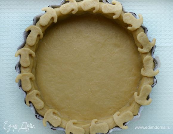 Достать тесто. Форму для выпечки застелить пекарской бумагой, смазать растительным маслом, если бумага без пропитки. Тесто раскатать в круг, диаметром, превосходящим диаметр формы см на 5, чтобы сделать бортики. Перенести круг в форму при помощи скалки. Края обрезать кулинарными ножницами. Края слегка придавить пальцами вовнутрь, чтобы получился красивый, ровный бортик. Оставшееся тесто пойдет на украшение. Выложить начинку и залить 2-мя взбитыми миксером яйцами.