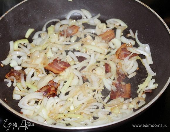 Бекон порезать на кусочки, обжарить на сковороде, добавить порезанный полукольцами лук, обжарить до золотистого цвета.